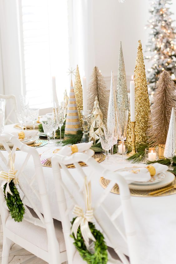 a beautiful gold and white Christmas tablescape with gold chargers, cutlery, gold and silver glitter cone Christmas trees, gold candleholders