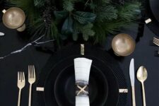a black table with black plates and chargers, lush evergreens and gold cutlery for a moody NYE tablescape