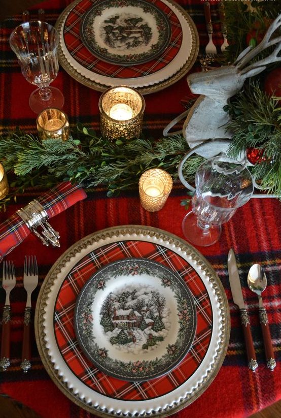 a bold traditional Christmas tablescape with a plaid tablecloth, chargers and napkins, greenery garlands, candles and chic burgundy cutlery