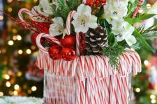 a bright Christmas centerpiece of a vase with candy canes, greenery, white blooms, snowy pinecones, candy canes and branches