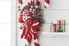 a bright Christmas decoration of oversized candy canes, foliage, berries, bright red and white ornaments and a large bow is lovely