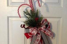 a bright door decoration of fir branches, bright bows and candy canes can be made in some minutes and looks fun and cool
