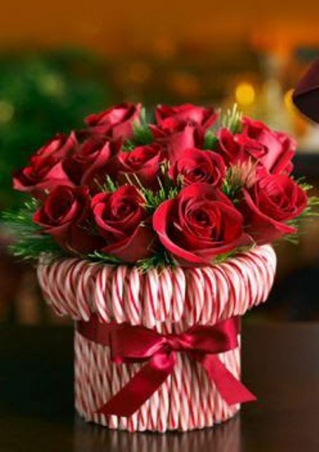 A bright holiday centerpiece  a vase wrapped with candy canes and with greenery and red roses is a very refined and chic idea