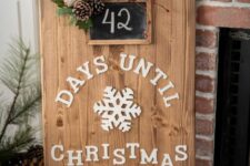 a cute Christmas sign of a wooden plaque with white letters, a red turck, evergreens, pinecones and a chalkboard house number