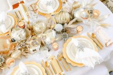 a dreamy glam gold and white Christmas tablescape with oversized ornaments, gilded leaves, chargers, cutlery and whte porcelain