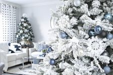 a flocked Christmas tree with blue, silver and black ornaments is a lovely and chic piece that looks frozen and elegant