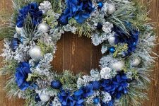 a frozen Christmas wreath with bold blue flowers, bows and silver and blue ornaments is a pretty and chic idea