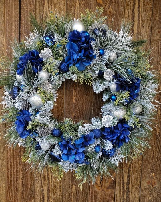 a frozen Christmas wreath with bold blue flowers, bows and silver and blue ornaments is a pretty and chic idea