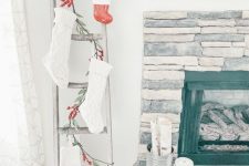 a ladder with evergreens and red berries, white stockings and a red Christmas ornament for holiday styling