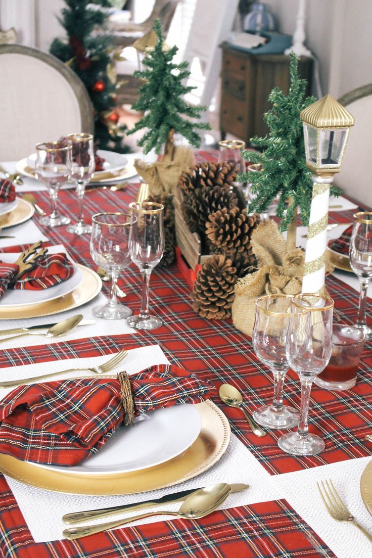 a lovely rustic Christmas tablescape with red plaid linens, gold chargers and cutlery, pinecones and mini fur trees wrapped in burlap