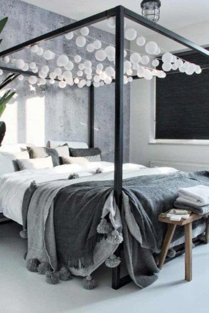 a monochromatic grey bedroom with a black canopy bed and string lights hanging over the sleeping space