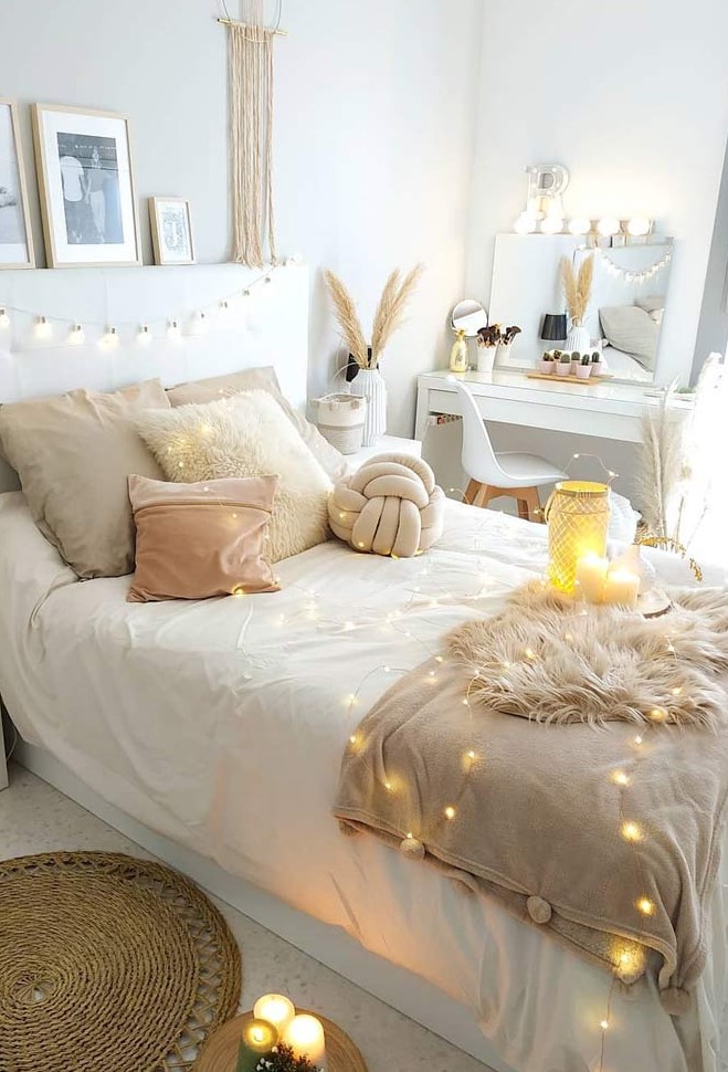 a neutral boho bedroom with a white bed with string lights, a sleek vanity with a mirror, macrame and fringe hangings