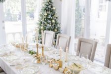 a pretty and bright holiday table setting with gold and white chargers, gold cutlery, white and gold ornaments, gold candleholders and white candles