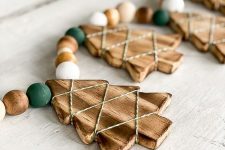 a rustic Christmas garland of wooden Christmas trees with twine, white, stained and green wooden beads is a pretty idea