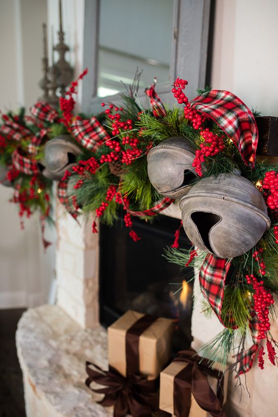 a rustic Christmas mantel with an evergreen garland with berries, red plaid ribbon and oversized bruch Christmas bells