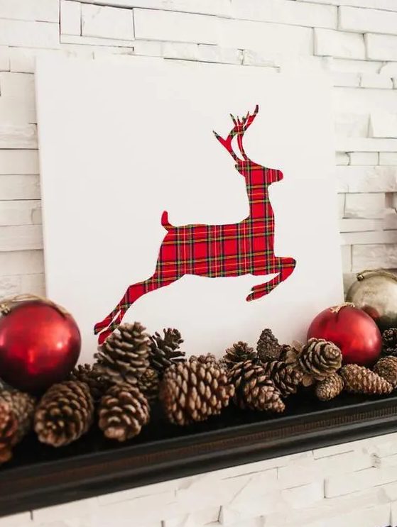 a simple white sign with a plaid deer plus red ornaments and pinecones for a cool mantel inspired by the holidays