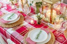 a stylish Christmas table with a red plaid tablecloth, gold lanterns, red and white blooms and woven placemats