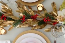 a stylish red and gold Christmas table with gold foliage, evergreens and berries, red blooms and candles