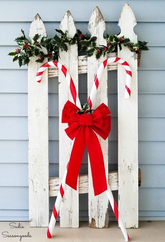 a vintage sleigh with greenery and candy canes accented with a large red bow is a pretty and cool rustic decoration for outdoors