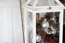 a white lantern with silver ornaments and usual and snowy pinecones is a gorgeous indoor or outdoor decoration for Christmas