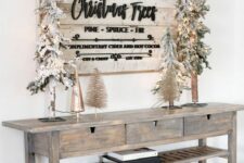 a whitewashed farmhouse Christmas sign with black letters and calligraphy, green wooden Christmas trees attached