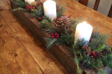 a wooden planter with evergreens, pinecones, berries and pillar candles is a lovely rustic Christmas centerpiece or decoration