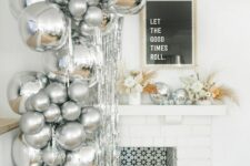 an arrangement of silver balloons next to the fireplace and in it, neutral florals and disco balls on the mantel for a NYE party