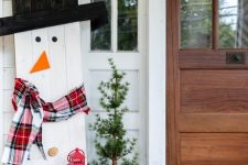 cozy and simple Christmas outdoor decor with a plywood snowman in a plaid scarf, with a top hat and red candle lanterns