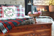 plaid bedding, a snowy evergreen and lights garland, a calligraphy sign, candles, a mini tree in a basket and a bowl with yarn balls and mini trees