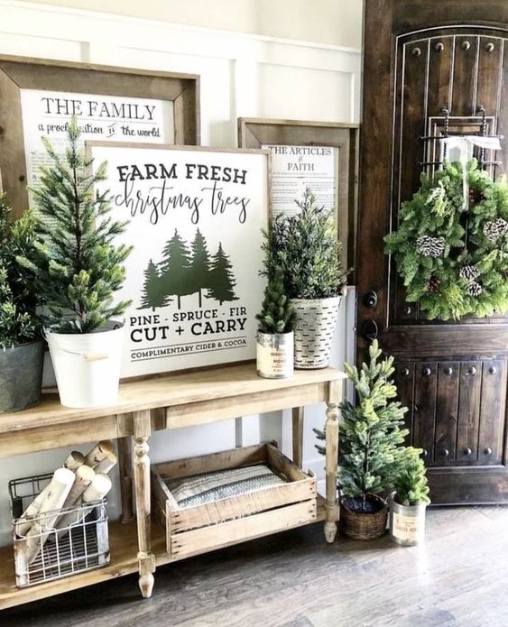 rustic Christmas entryway decor with lots of Christmas trees in buckets, vintage artworks, crates and baskets with firewood