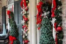 Christmas topiaries with red bows, lanterns with lights, an evergreen garland with red ribbons and lights and red ornaments