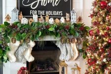 a Christmas mantel with an evergreen and snowy pinecone garland, mini houses and stockings plus a Christmas tree with matching decor