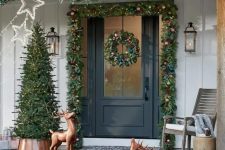 a bold Christmas porch with evergreen garlands with bold ornaments, copper deer, a Christmas tree with lights and star lights over the space
