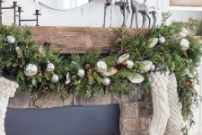 a cottage Christmas mantel with an evergreen, pinecone and ornament garland, neutral stockings, silver deer and candles in a black candelabra
