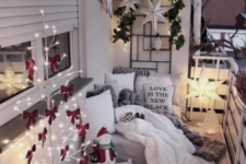 a cozy little balcony with a light tree with red bows, some candle lanterns, a star lamp, stars and greenery on the wall and fur and knit textiles