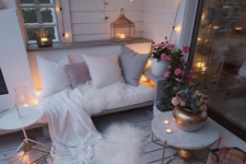 a cozy winter balcony with faux fur, candles in lanterns and candleholders, lights and potted blooms