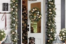a festive Christmas porch with wooden candle lanterns, an evergreen garland with metallic ornaments and a matching wreath on the door