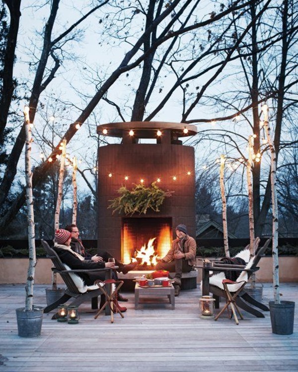 a gorgeous winter terrace with a large fireplace, wooden chairs and a vintage table, candle lanterns and string lights