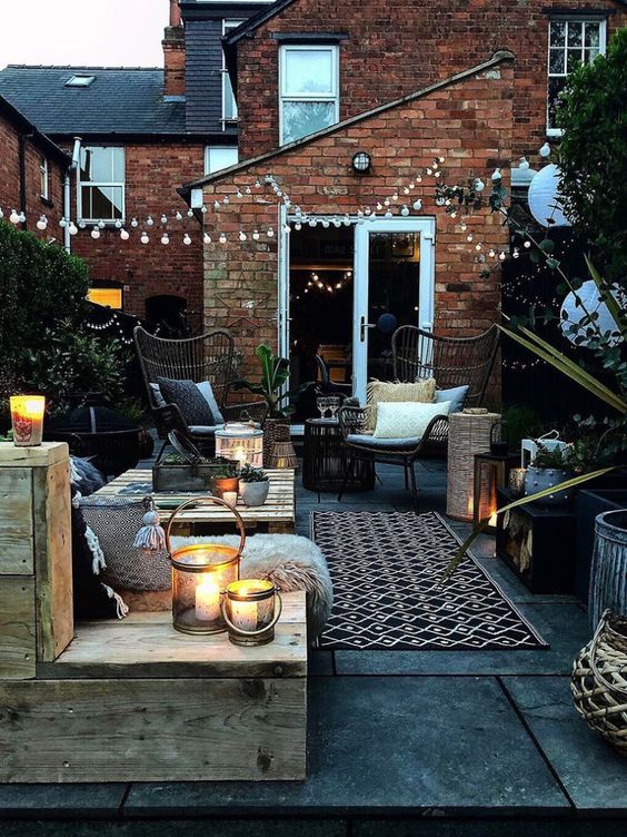 a lovely winter patio in boho style, with wicker chairs, a pallet coffee table and wooden furniture, faux fur and candle lanterns