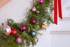 a lush evergreen and colorful Christmas ornament garland with red bows is a cool railing decor idea