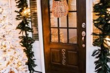 a lush evergreen garland with lights over the door, a flocked Christmas tree in a crate and a basket with greenery
