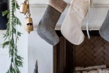 a modern Christmas mantel with a greenery and pinecone garland, bells, stockings and a pompom garland for a touch of fun