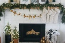 a modern glam Christmas mantel with an evergreen and light garland, white stockings, mini bottle cleaner trees and winter photos plus a bell garland