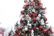 a pretty and bright white and red Christmas tree with snowflakes, cages, houses, snowmen, deer and an elf hat Christmas tree topper