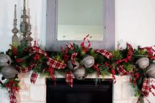 a vintage farmhouse Christmas mantel with an evergreen, oversized bell and red plaid ribbon garland, metal candleholders and gift boxes