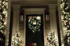an evergreen and light garland, mini Christmas trees and a wreath make the porch very Christmassy and welcoming