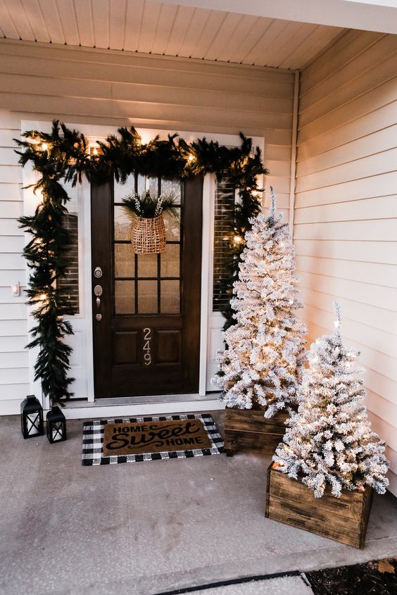 an evergreen and light garland over the door, flocked Christmas trees with lights in crates for a Christmas farmhouse porch