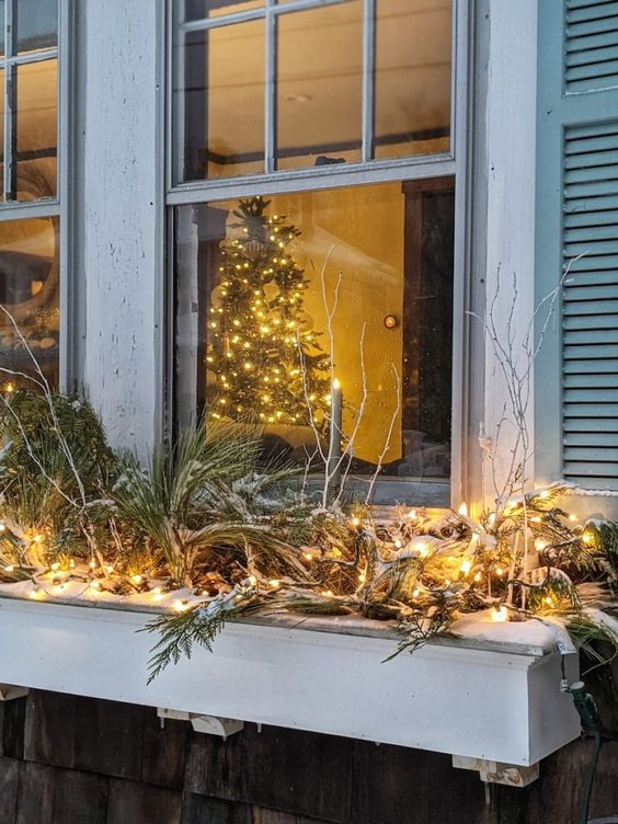 an outdoor window box with evergreens, vine, pinecones and lights is a cool way to the exterior of your house for Christmas