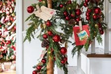 beautiful Christmas banister decor with an evergreen garland, red ornaments, pinecones and Christmas postcards