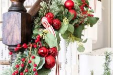 chic Christmas banister decor with evergreens and foliage, red ornaments, berries and a red and white striped ribbon is cool